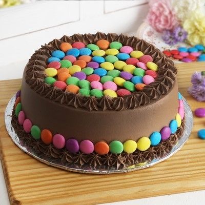 there is a chocolate cake with colorful candies on the top and bottom, sitting on a wooden table