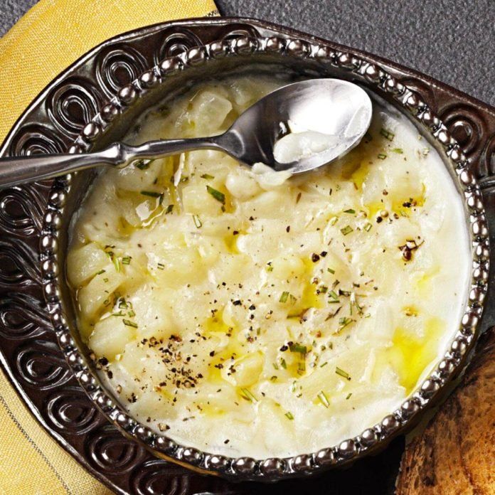 a bowl filled with potatoes and herbs on top of a wooden table next to a spoon