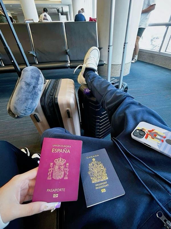 a person is holding a pink passport and sitting in an airport with their feet on the luggage