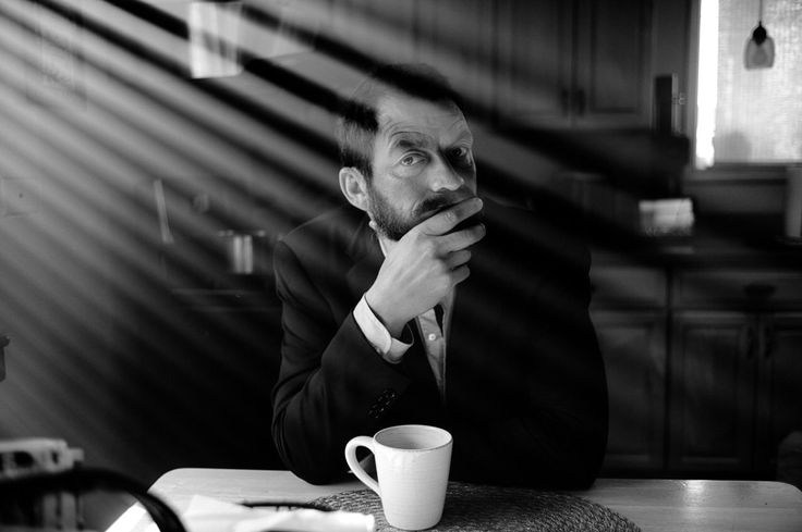 a man sitting at a table with a coffee cup in front of him and his hand on his chin