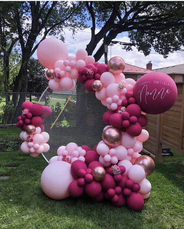 pink and gold balloons are arranged in the shape of a wreath on top of grass