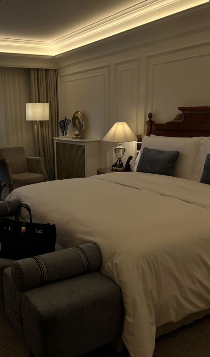 a hotel room with a large bed, chair and lamp on the nightstands in front of it