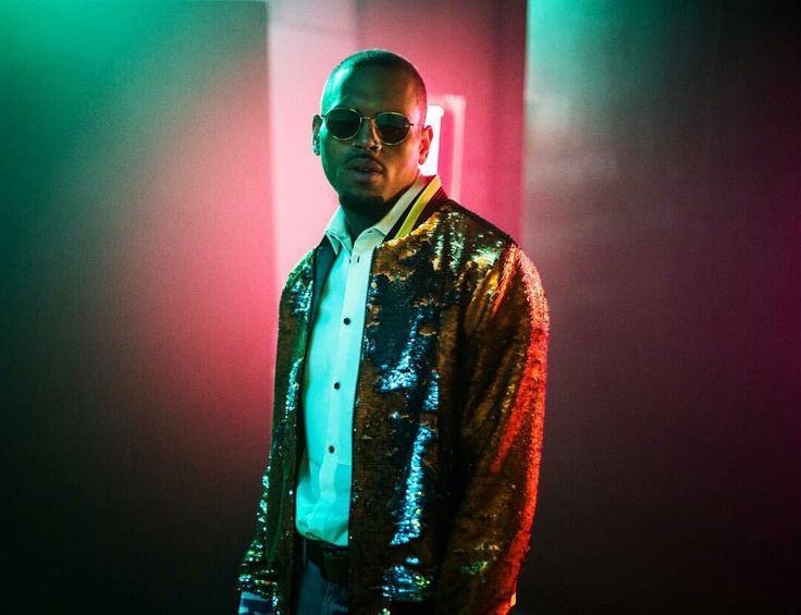 a man wearing sunglasses standing in front of some colored lights and looking at the camera