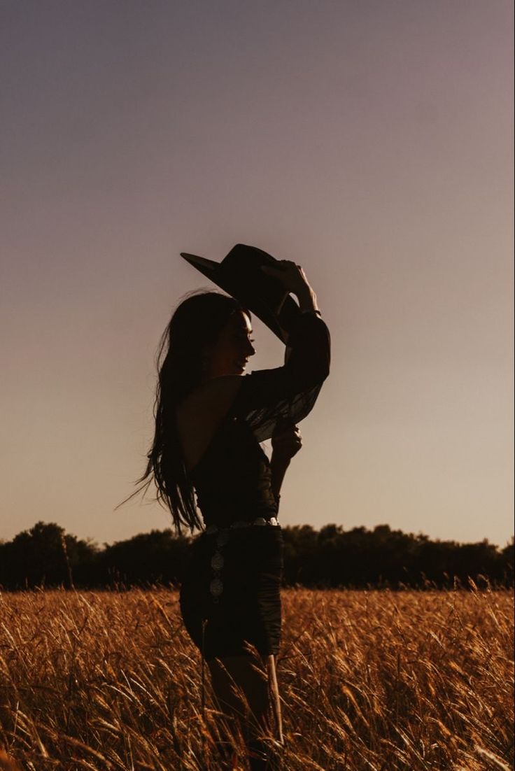 a woman standing in a field holding her hat