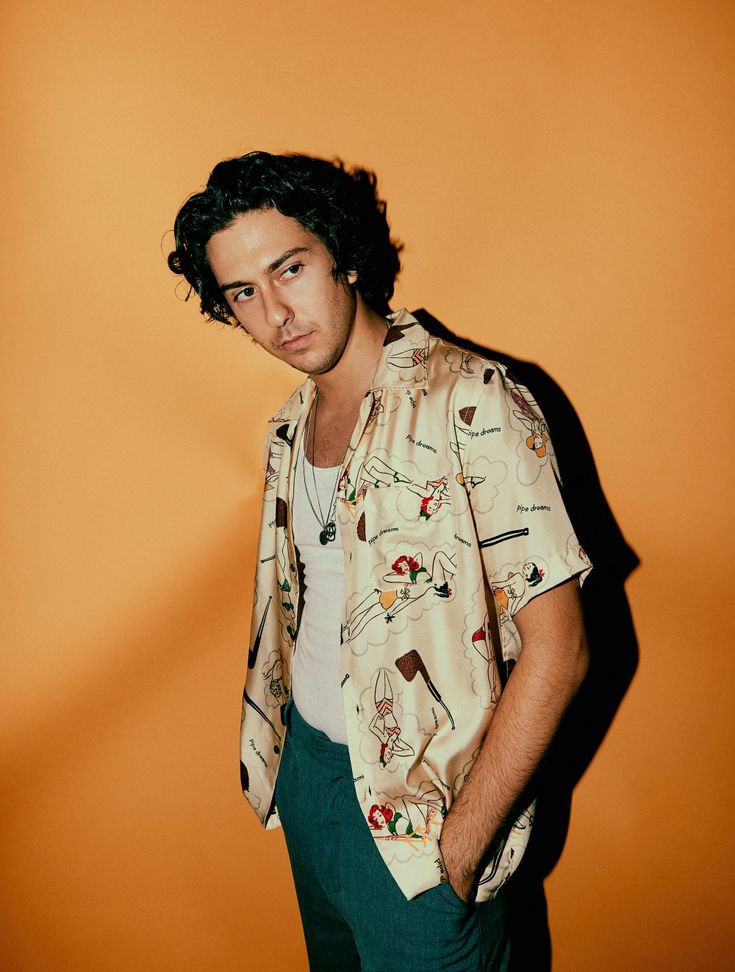 a man standing in front of an orange wall wearing a shirt with pictures on it