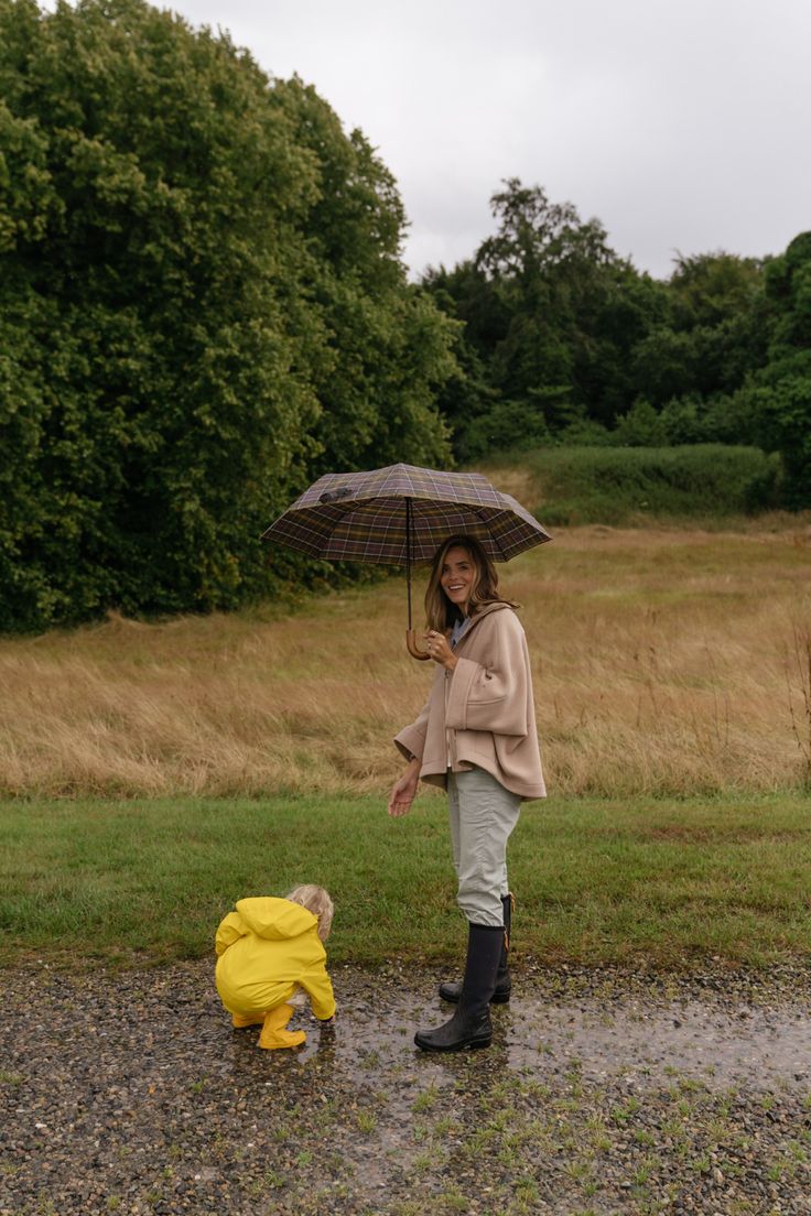 a woman holding an umbrella standing next to a small yellow dog on a gravel road