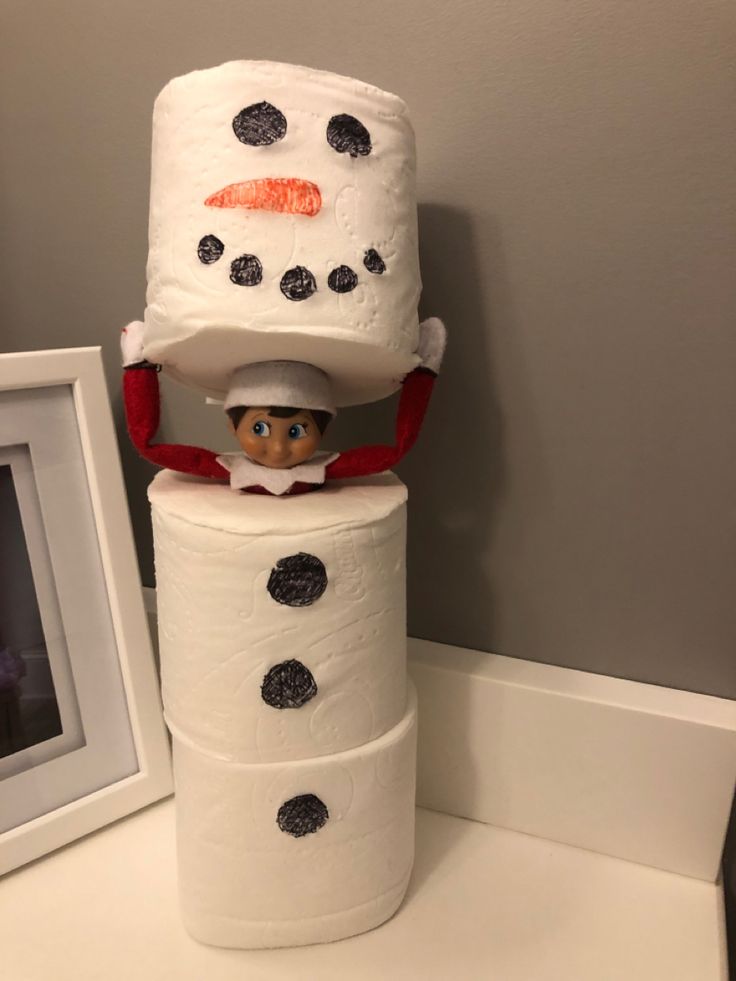 an elf is sitting on top of two rolls of toilet paper with a snowman hat