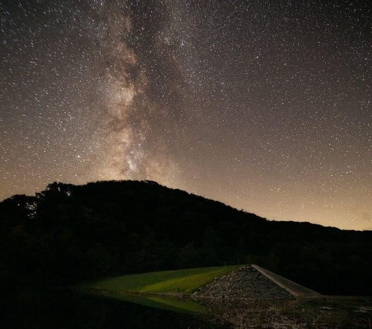 the night sky is filled with stars above a hill