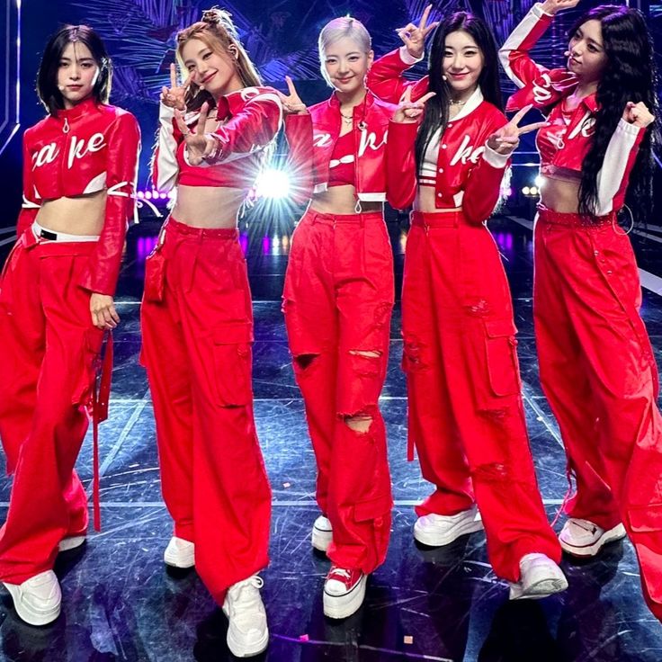 girls in red outfits on stage with one pointing at the camera and two standing behind her