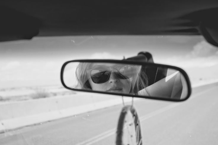 a woman is seen in the rear view mirror as she drives down the road with her sunglasses on