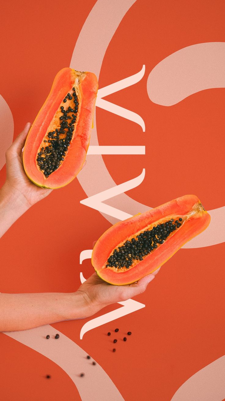 two pieces of papaya being held up against an orange background