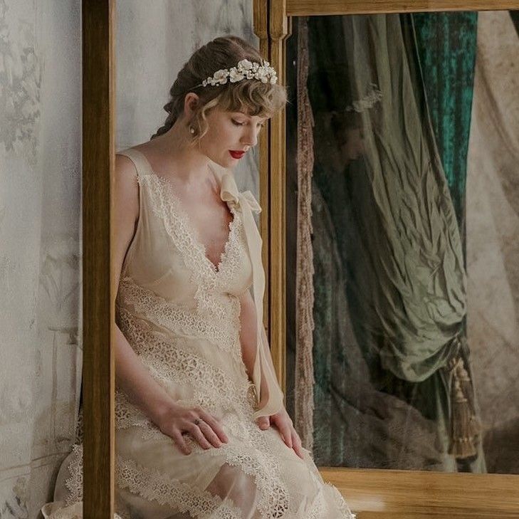 a woman sitting on a bed looking at herself in the mirror, wearing a wedding dress