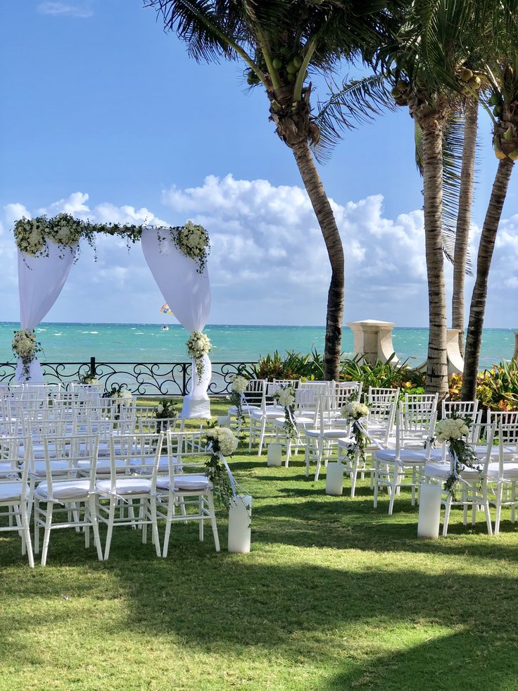 an outdoor wedding set up with white chairs and flowers on the aisle, overlooking the ocean