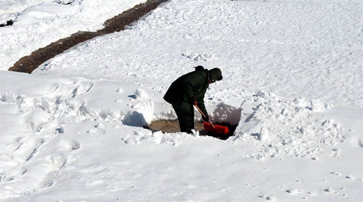 a man shoveling snow with a red bucket