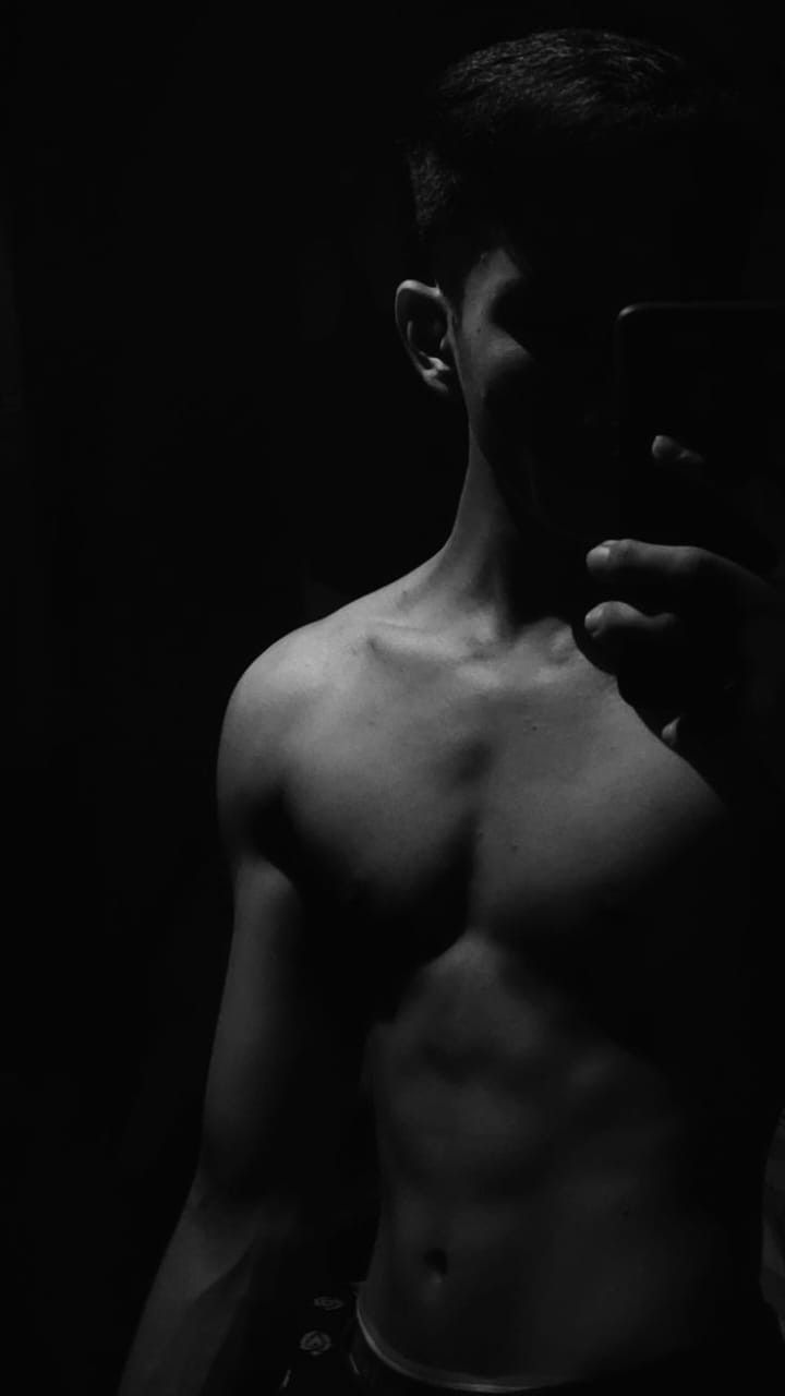 a shirtless man taking a selfie in the dark with his cell phone to his ear