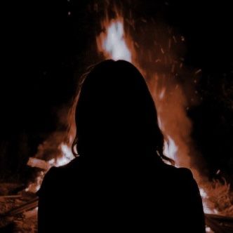 a woman standing in front of a fire with her back turned to the camera,