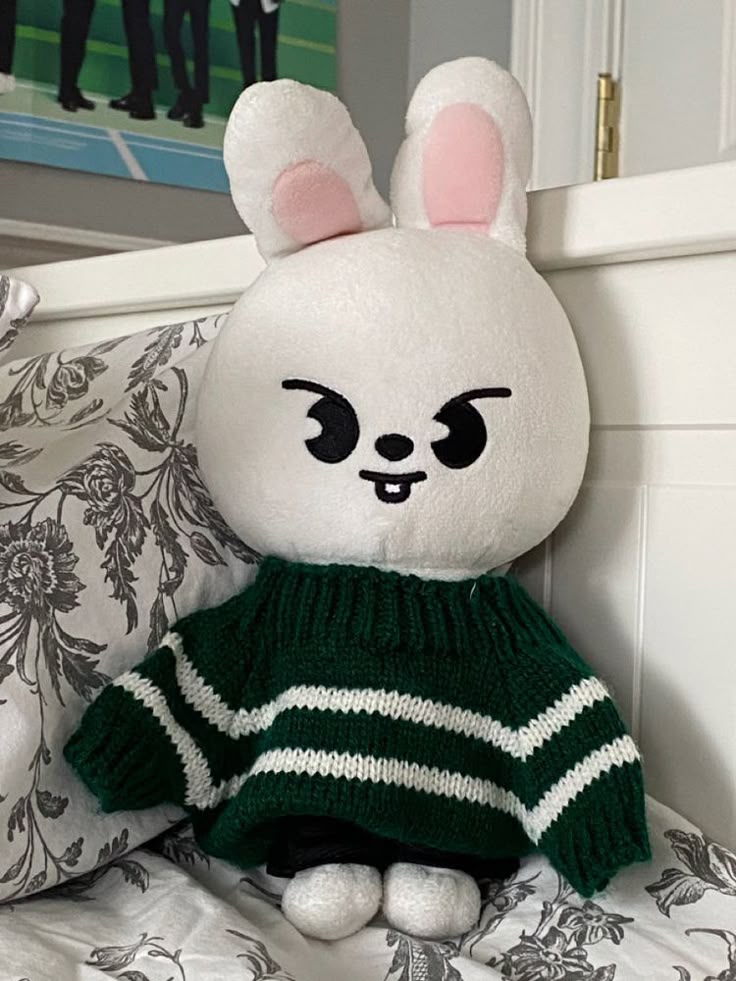 a stuffed animal wearing a green sweater sitting on top of a bed