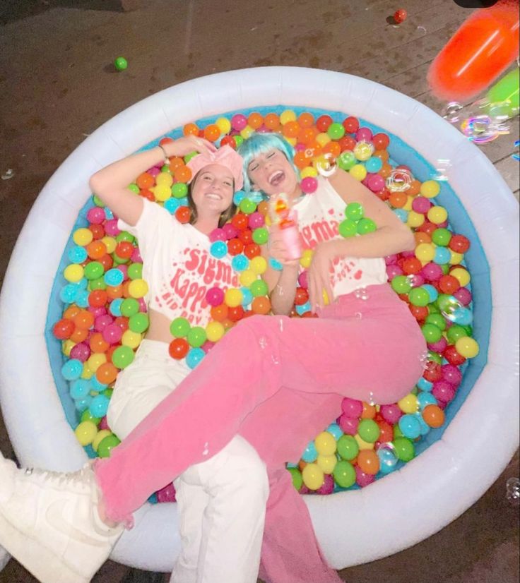 two women laying in an inflatable ball pit with gummy balls on the floor