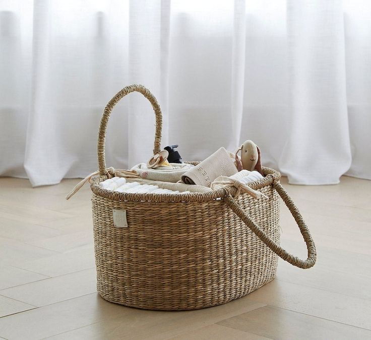 a wicker basket with two dolls in it on the floor next to a window