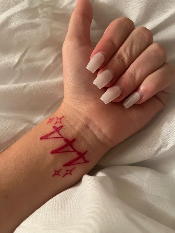 a woman's hand with a red tattoo on her left wrist and white nails