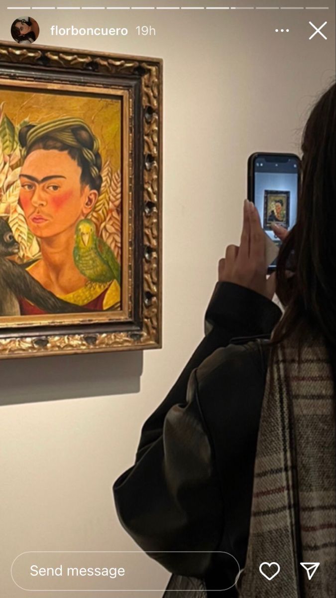 a woman taking a photo of a painting on the wall with her cell phone in front of her