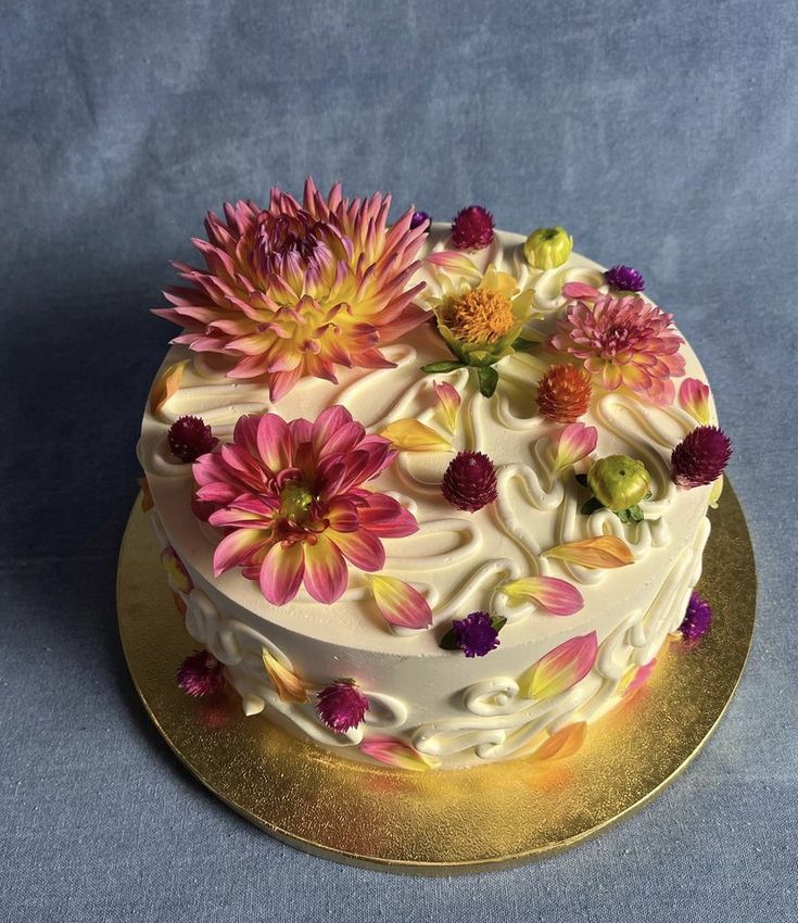 a white cake with pink and yellow flowers sitting on top of a gold platter