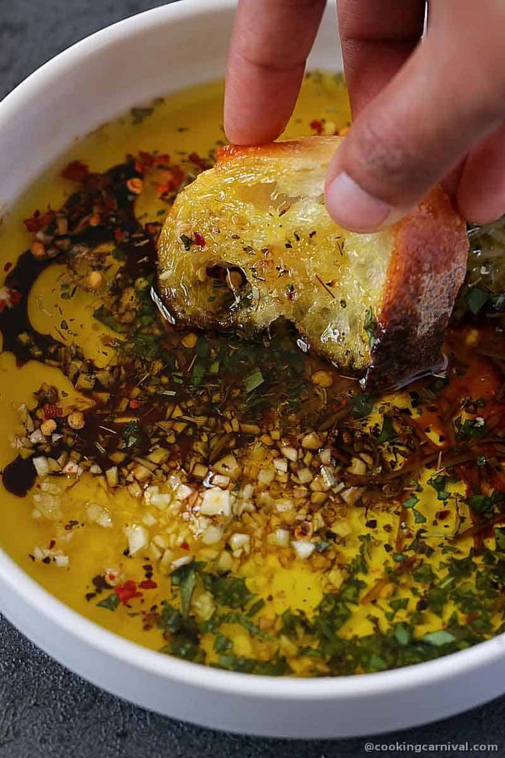 a person dipping food into a white bowl filled with broth and other things in it