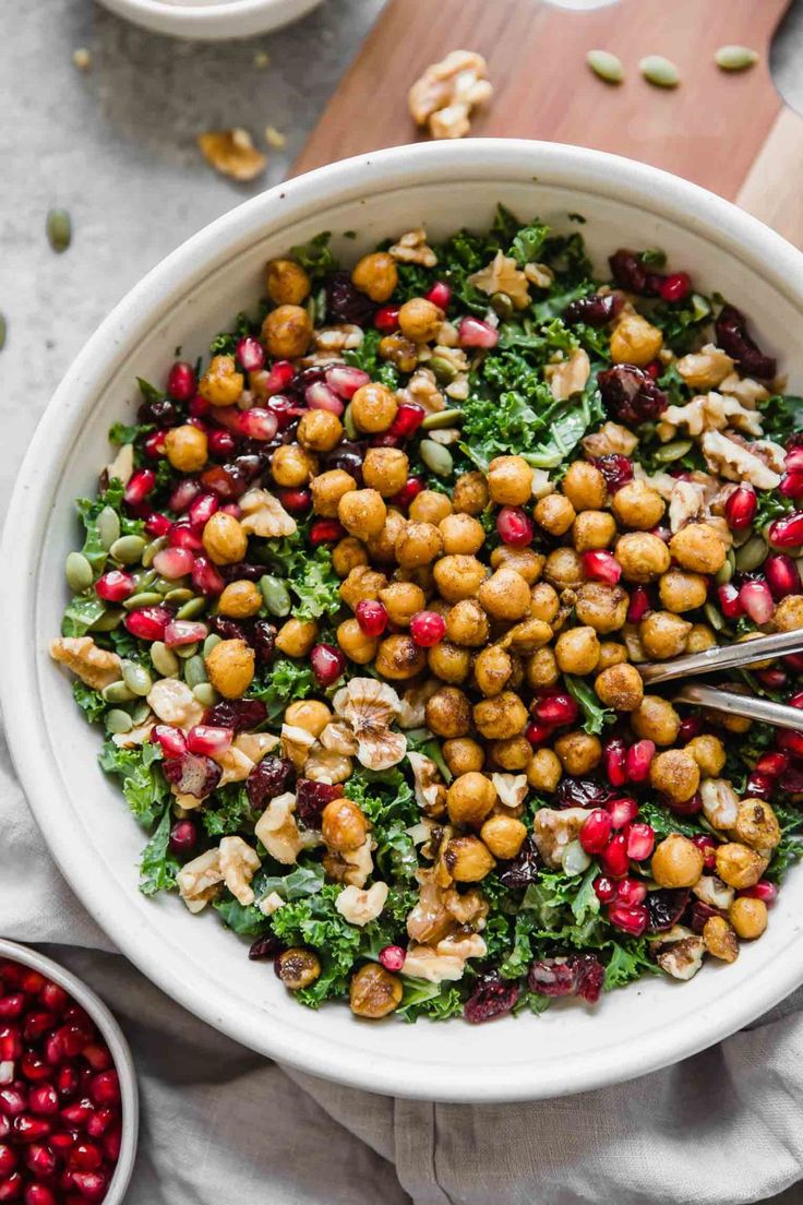 a white bowl filled with chickpeas, pomegranates and nuts