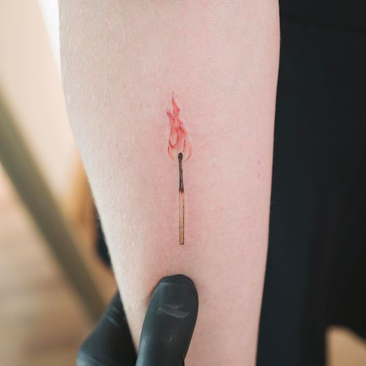 a person with a small tattoo on their arm holding a lit match in one hand