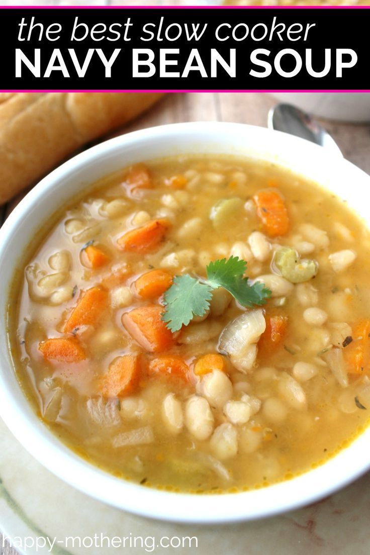 a bowl of soup with carrots, beans and parsley in it next to a loaf of bread