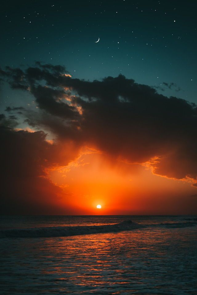 the sun is setting over the ocean with dark clouds and stars in the night sky