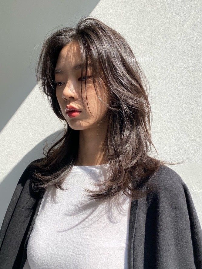 a woman standing in front of a white wall with her hair blowing in the wind