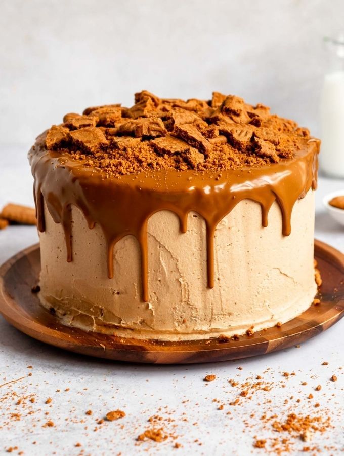 a cake with chocolate icing and nuts on top sitting on a plate next to a glass of milk