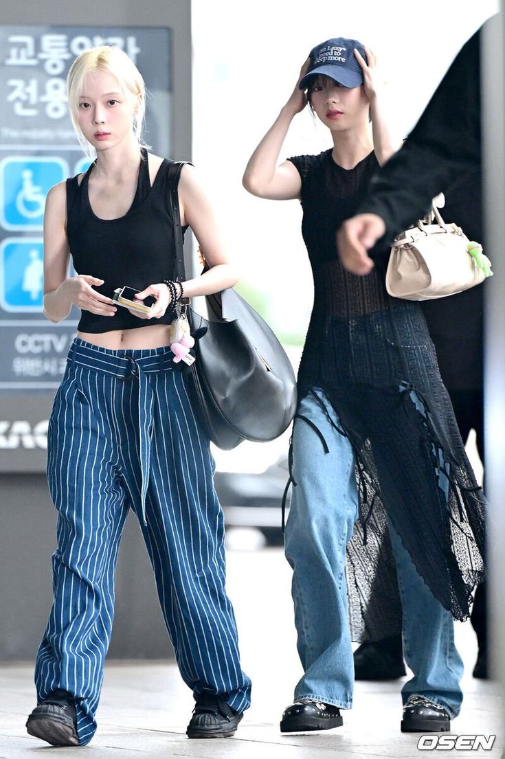 two young women walking down the street with one holding her hand on her head and another carrying a purse