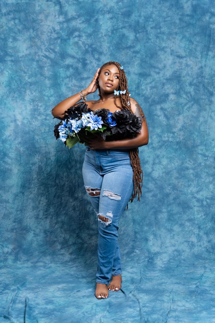 a woman standing in front of a blue backdrop with flowers on her chest and arms behind her head