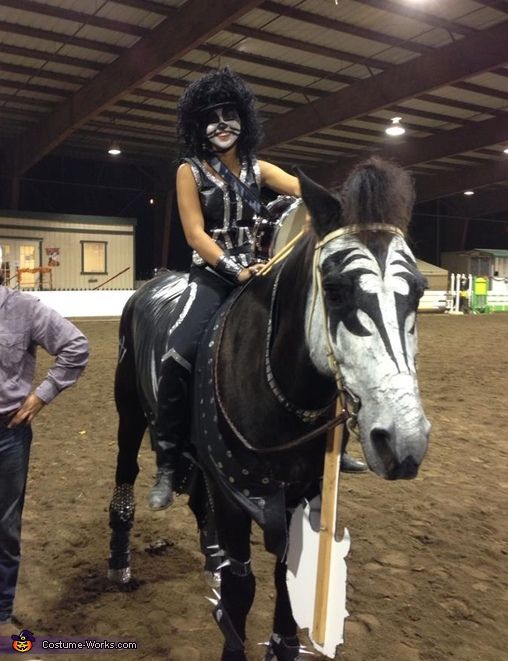 a woman in costume riding on the back of a black and white horse while standing next to a man