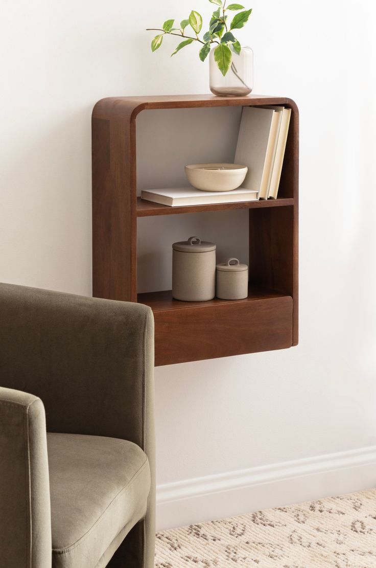 a book shelf with two books on it next to a chair and potted plant