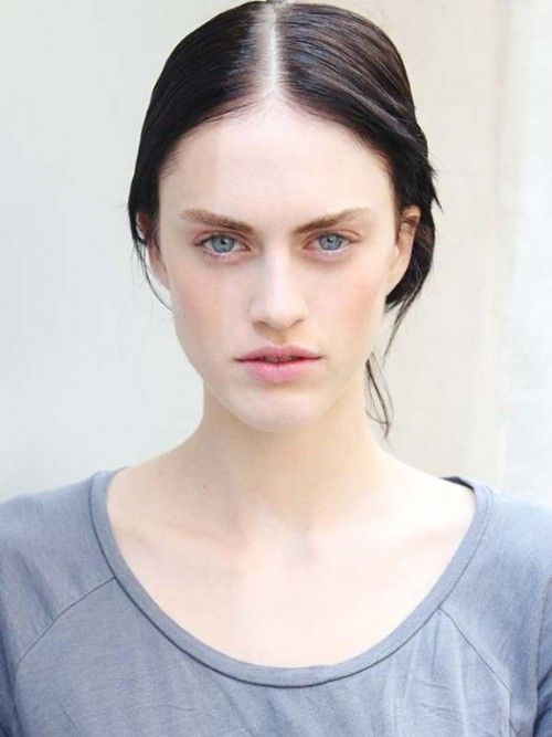 a woman with dark hair and blue eyes is looking at the camera while wearing a gray shirt