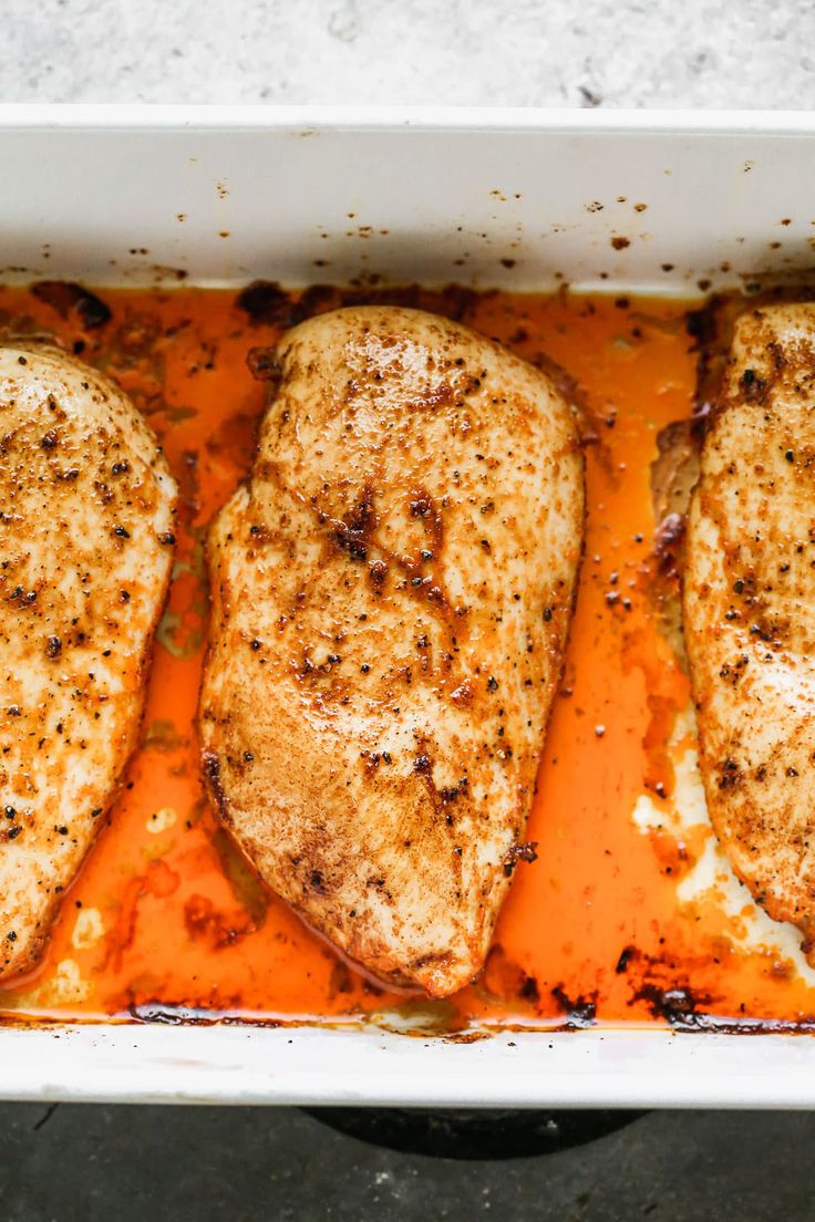 three pieces of chicken in a white casserole dish with orange gravy