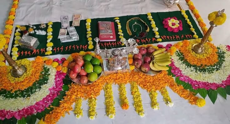 an arrangement of fruits and flowers on a white table cloth with green trimmings