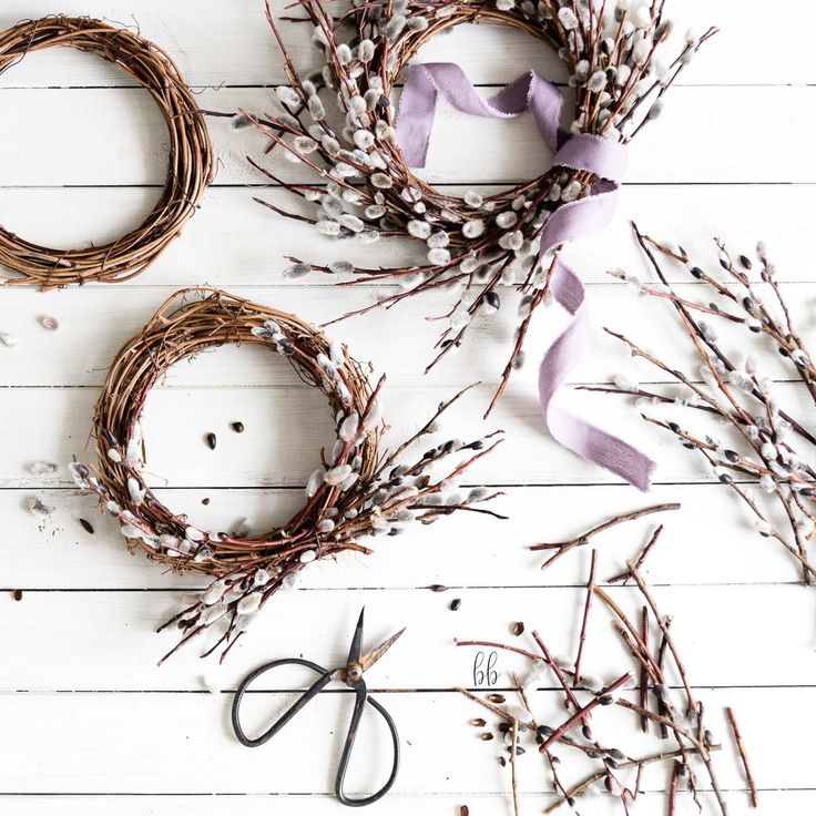 three wreaths with purple ribbons and scissors on a white wooden surface next to each other