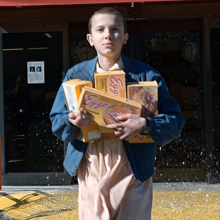 a young boy holding two pizza boxes in front of a storefront with water sprinkles on it