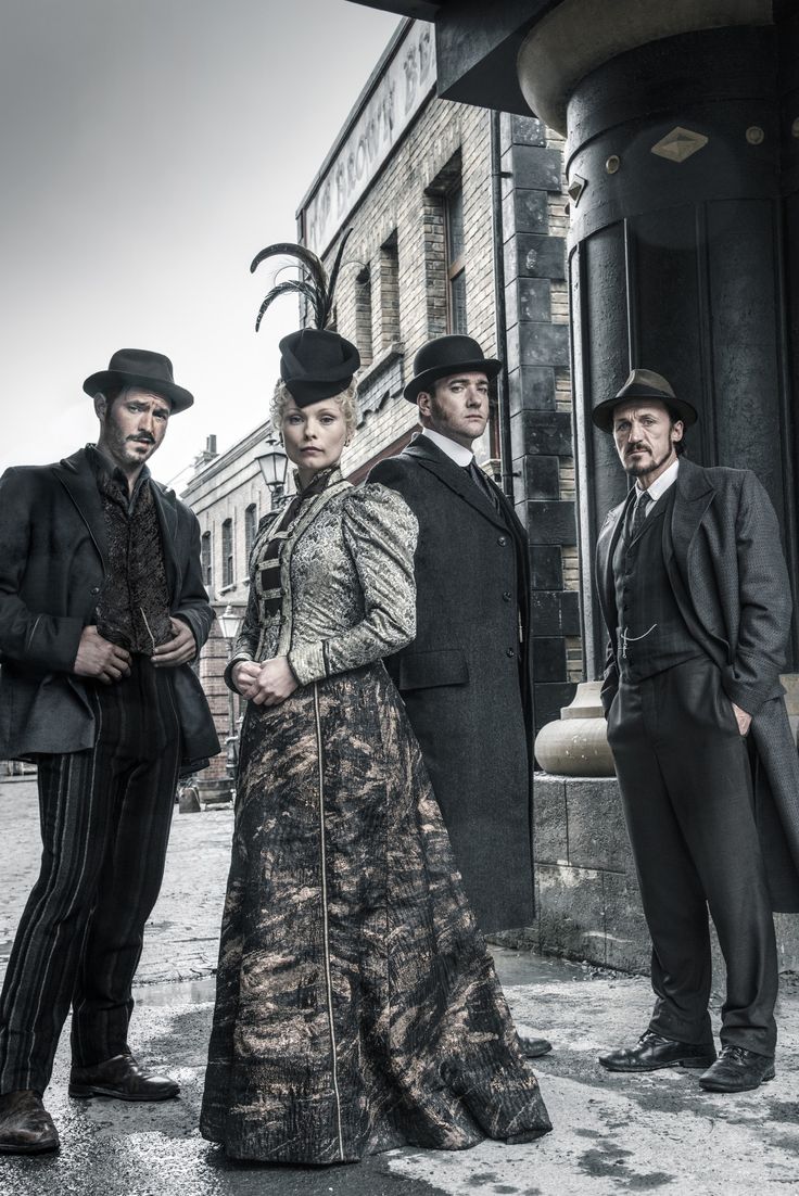 three men and a woman standing in front of an old building wearing period clothing with hats on their heads