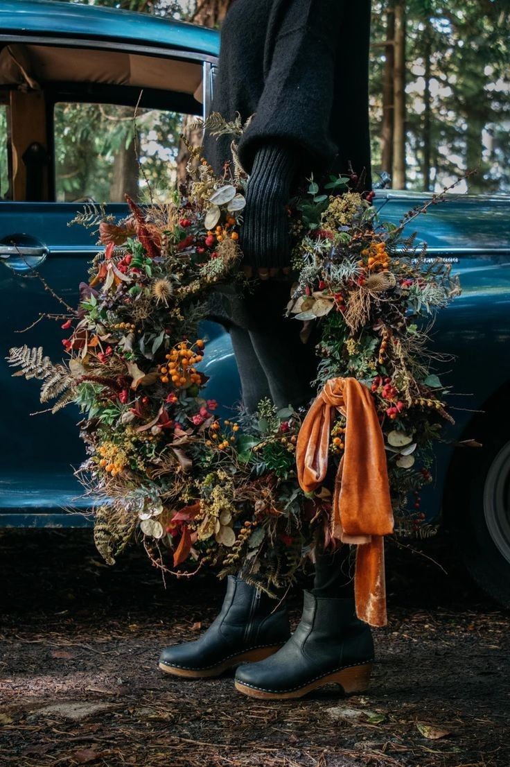 a person standing in front of an old blue car with a wreath on the door