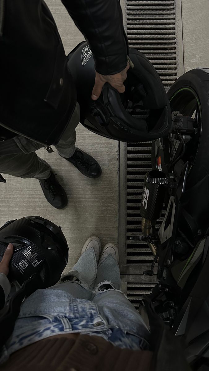 two people standing next to each other with their feet on the ground and one person sitting in front of a motorcycle