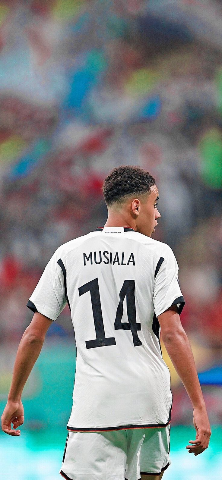 a soccer player is standing in front of the crowd with his head turned to look down