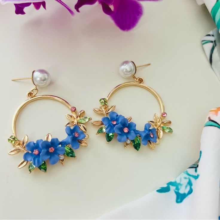 These Stunning Hoop Earrings Showcase A Vibrant Floral Design, With Delicate Blue Flowers Adorned With Pink And Green Crystals. The Golden Hoops Are Accented With Elegant Leaf Details And Are Topped With A Lustrous Pearl Stud, Adding A Touch Of Sophistication. These Earrings Are Perfect For Those Who Love Bold And Colorful Accessories, Making Them A Beautiful Statement Piece For Both Casual And Formal Occasions. Their Playful Yet Refined Style Is Sure To Bring A Fresh And Lively Vibe To Any Outf Blue Flower Shaped Earrings For Summer, Blue Flower-shaped Summer Earrings, Blue Earrings With Flower Charm For Spring, Summer Jewelry With 3d Flower Shapes, Blue Dangle Flower Earrings For Spring, Blue Flower Charm Earrings For Spring, Spring Blue Flower Earrings, Blue Flower Earrings For Spring, Blue Spring Earrings