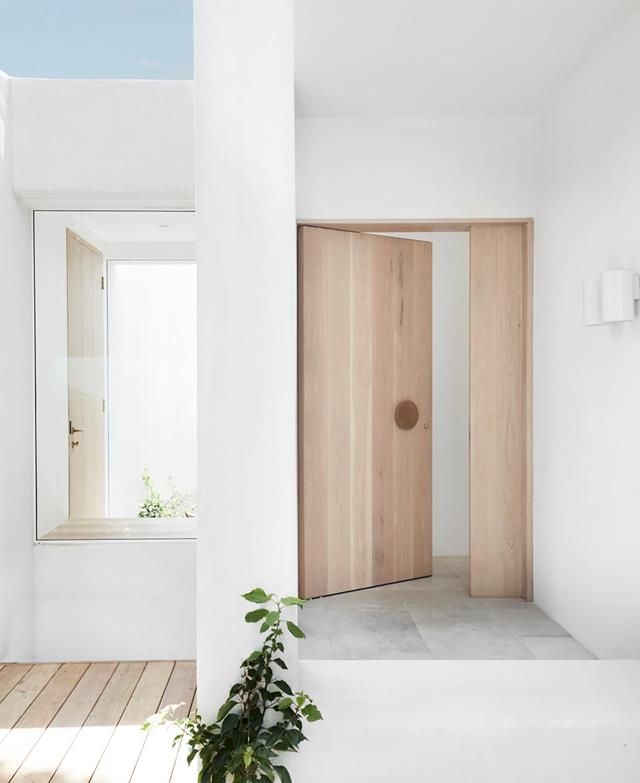 an open door in a white room next to a wooden floor and plant on the ground