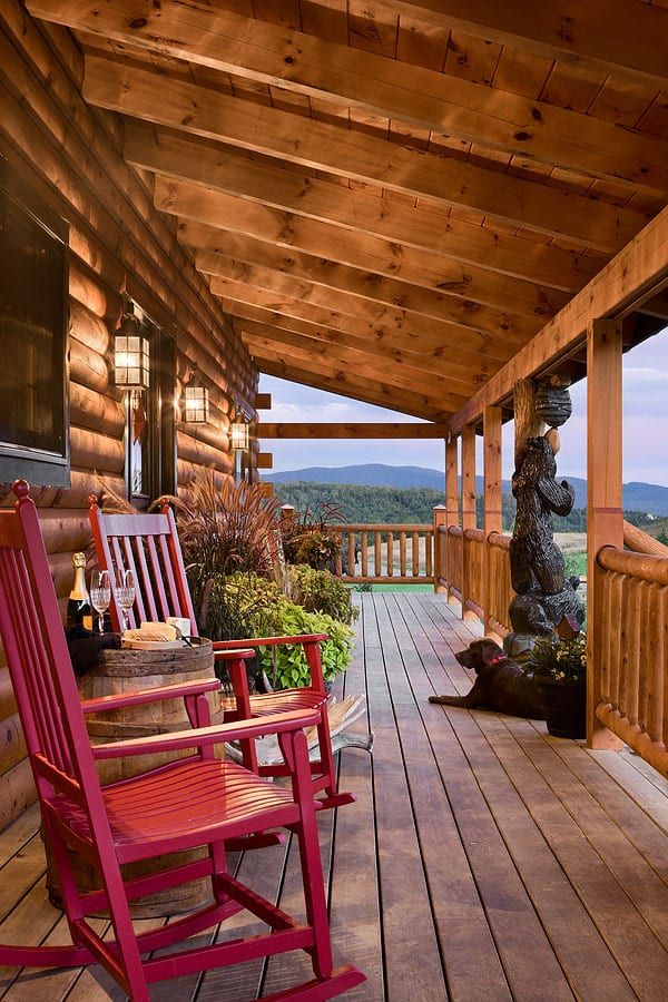 two red rocking chairs sitting on top of a wooden porch next to a stone statue