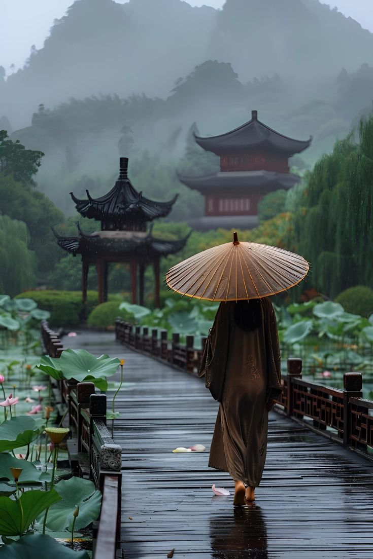 a woman with an umbrella walks down a path in the rain near pagodas and water lilies